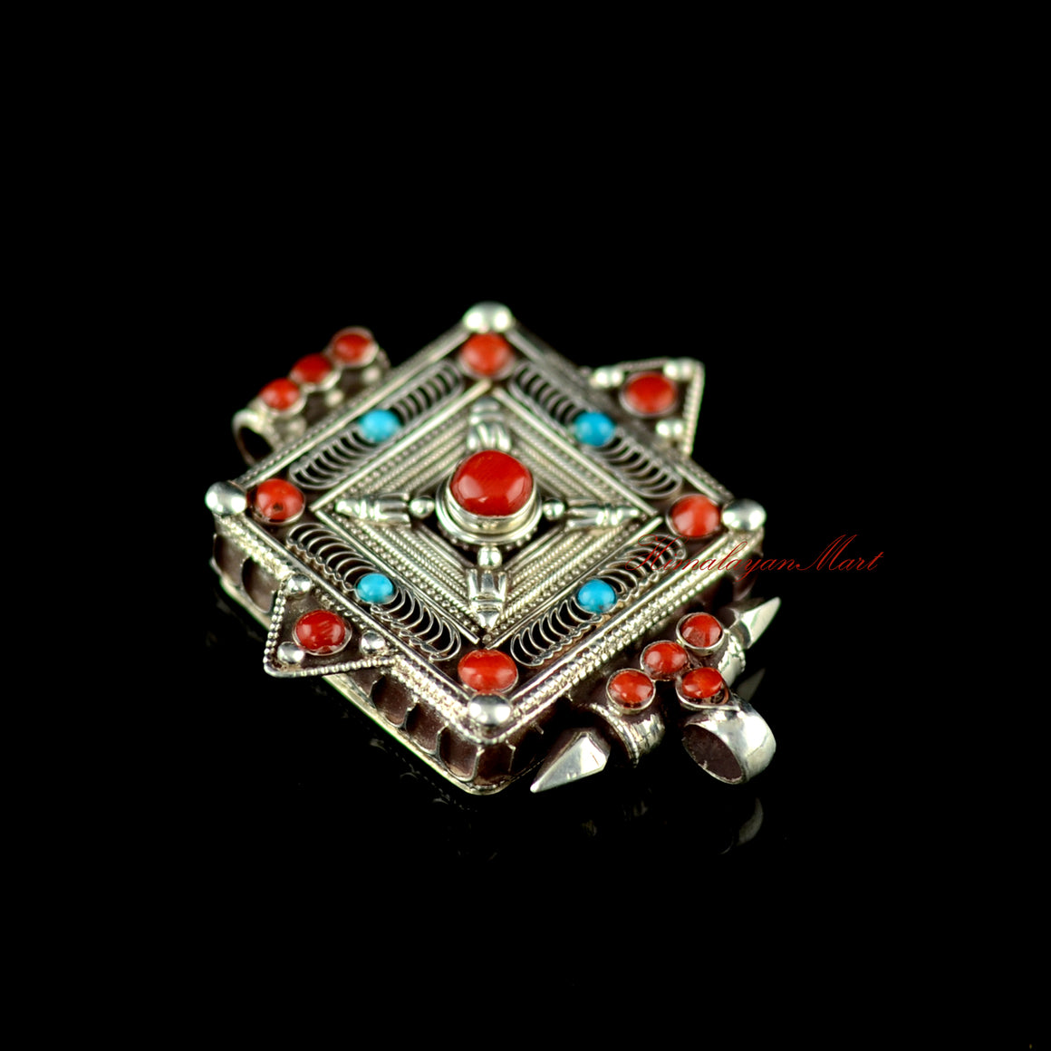 Angled lower-right view of the Buddhist silver pendant highlighting gemstone inlay and siko filigree carving.