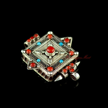 Angled lower-right view of the Buddhist silver pendant highlighting gemstone inlay and siko filigree carving.