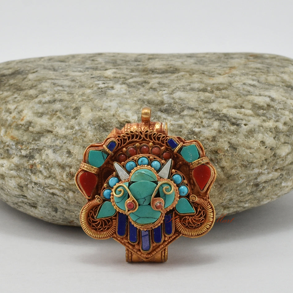 Top-down view of handcrafted Chhepu Face Ghau prayer box pendant, showing detailed carvings and gemstone decorations.