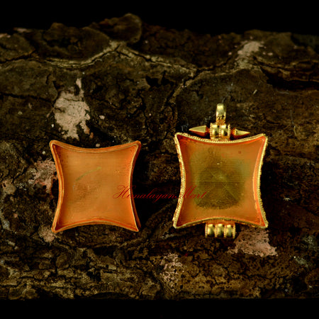 Opened Tibetan gemstone pendant revealing interior details, silver filigree, and coral and emerald accents.